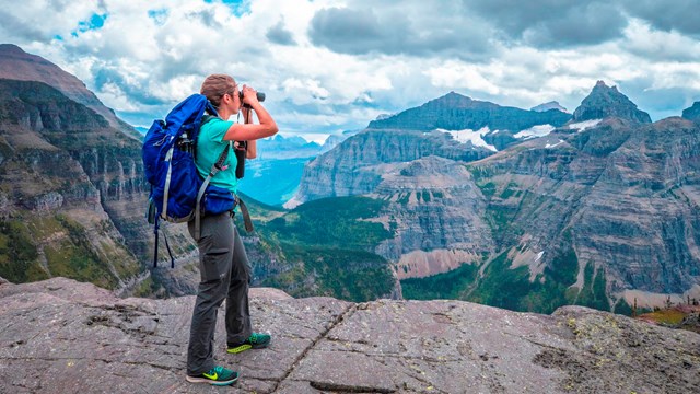 A person wearing a backpack looks out at a mountain landscape. 