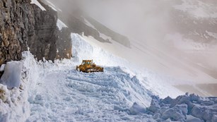 A tractor plows snow in the mountains.