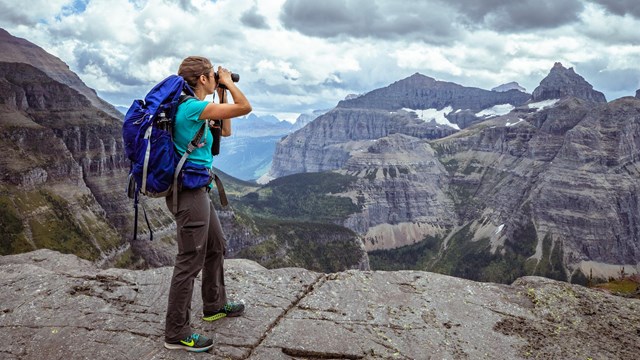 A person wearing a backpack looks out at a mountain landscape. 