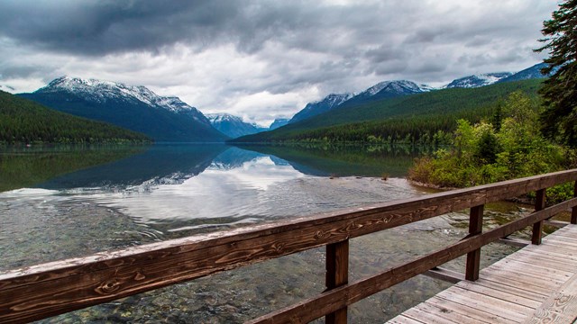 Bridge in front of a mountain reflecting in Bowman Lake on a summer day.