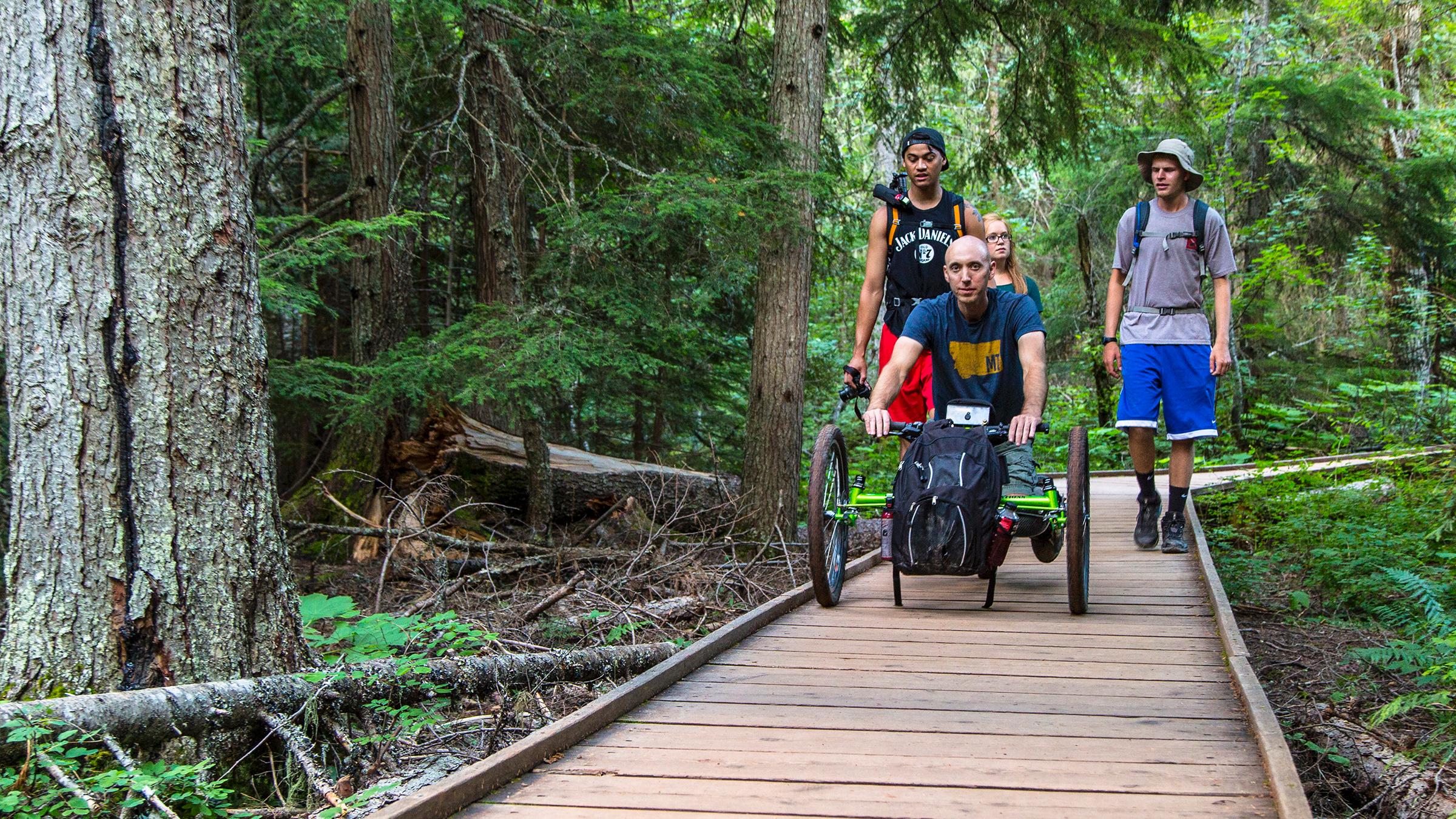 Off-road wheelchair and group on the accessible Trail of the Cedars boardwalk.