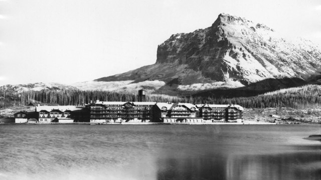 Historic image of long hotel building on lakeshore below mountain peak
