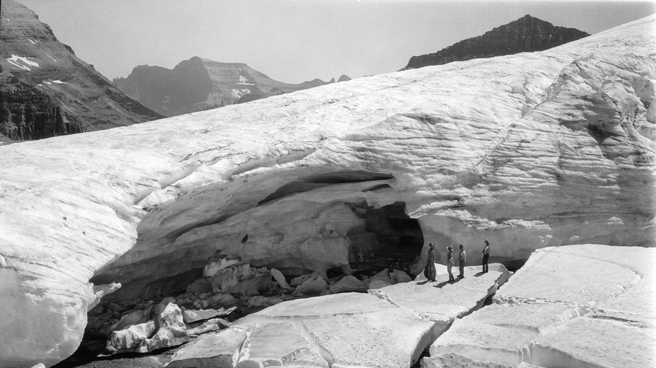 People stand on ice near a glacial cave in the mountains. 