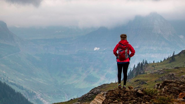 A hiker stands on a rock in the mountains with a vast landscape beyond them.