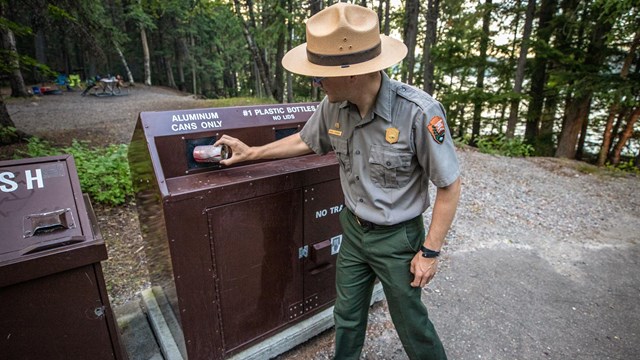 A park ranger puts a can into a recycling bin. 