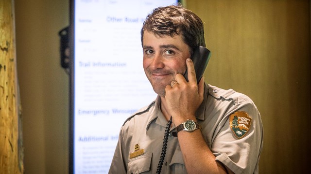 A park ranger smiles while talking on the phone. 