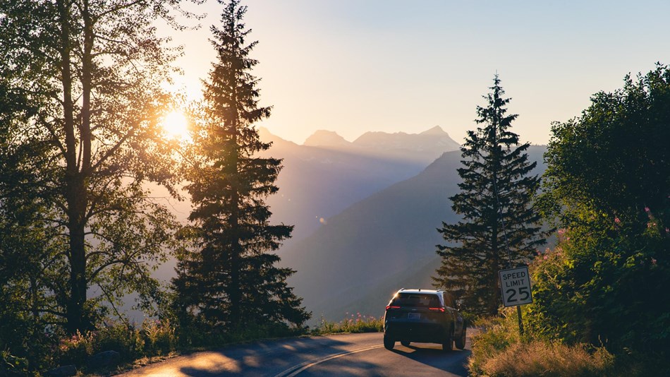 A car drives down a mountain road at sunset. 