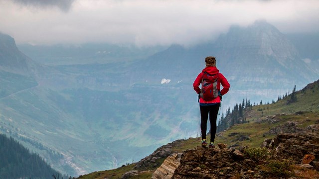 A hiker stands on a rocky hill with a vast view beyond them.