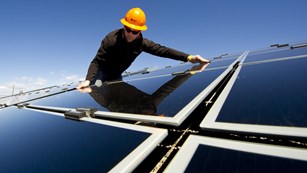 A person in a hardhat adjusts a solar panel. 