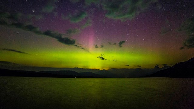 beams of light, colors, and clouds in night sky over lake