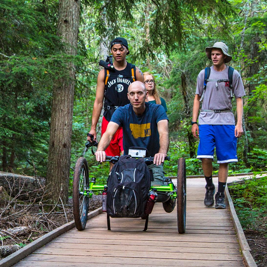 Off-road wheelchair and group on the accessible Trail of the Cedars boardwalk.