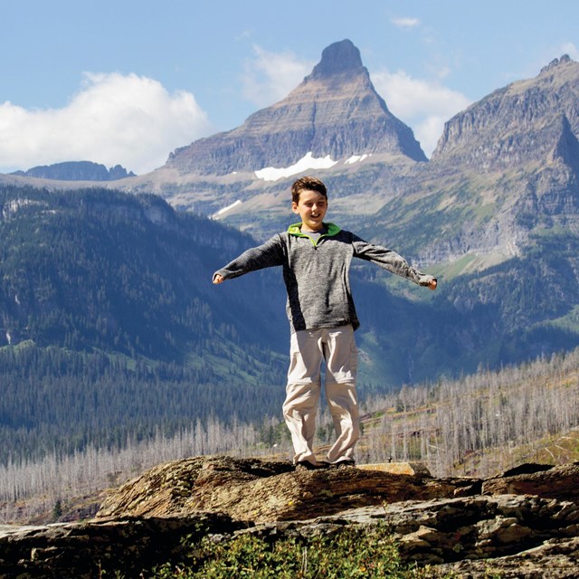 A young boy stands on a rock with the wind whipping at his clothes.