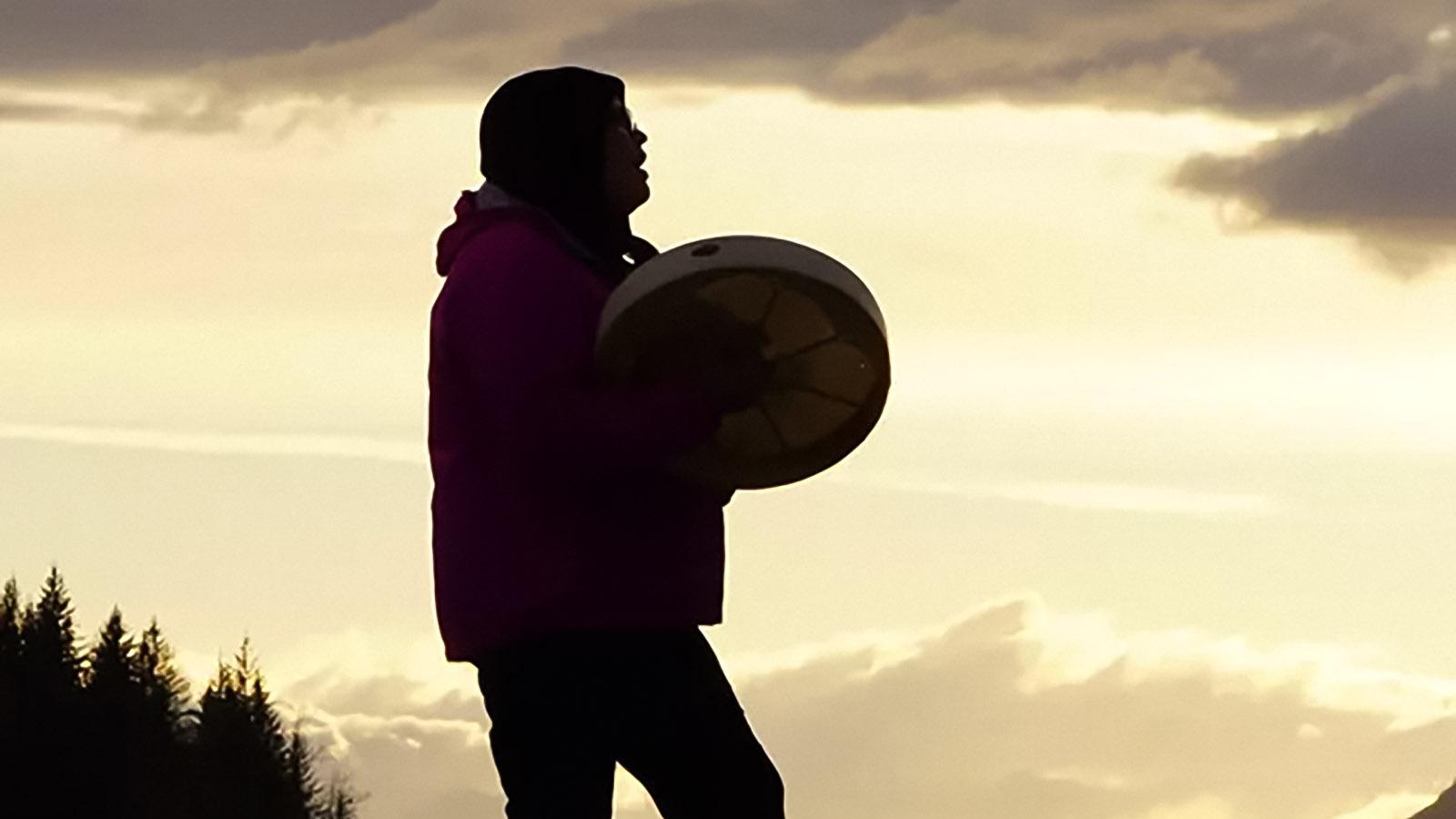 Łingít drummer silhouetted against sunset sky