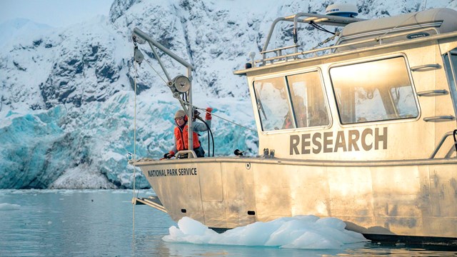 A park ranger works a rope pulley device on a research boat in front of Margerie Glacier