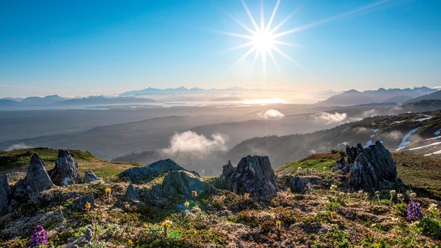 A bright sun illuminates a vast scene of distant forests and mountains