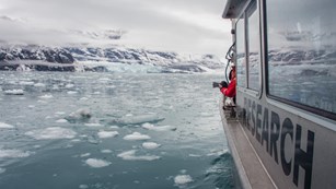 a research boat floats through icy-filled water near a glacier