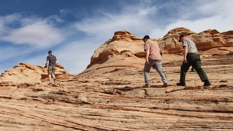 Ranger and visitor hike over twisting, layered sandstone