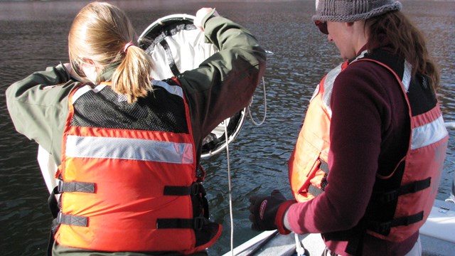 Researcher leans over side of boat to pull up equipment