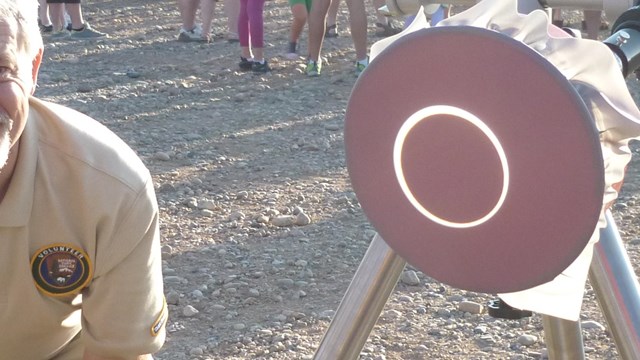 Solar scope displaying projected image of an eclipsing sun on a dark background. Volunteer ranger st