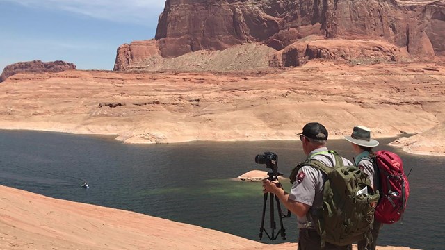 Two rangers, one holding a camera, standing on sandstone cliff