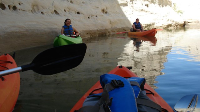 Multicolored kayaks in and out of the shadows on the lake.