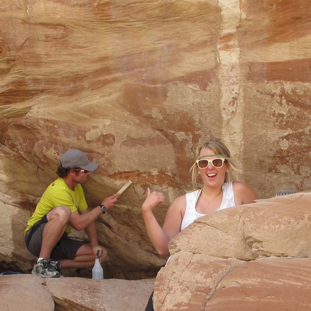 A man and a woman clean graffiti on a sandstone wall.