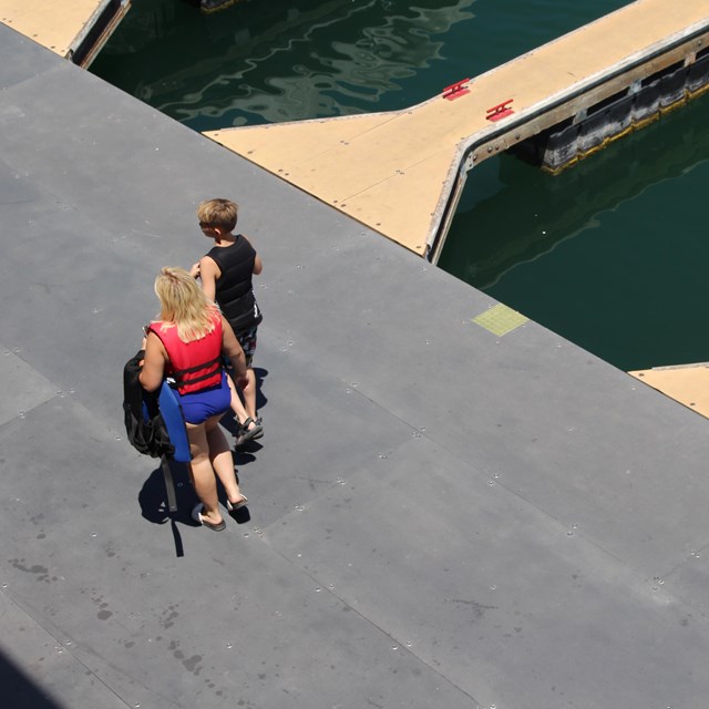 Overhead view of woman and child wearing life jackets walking down dock by empty boat slips