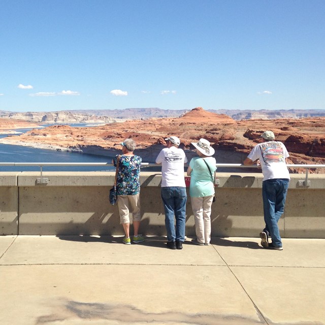 Group of people stand at railing overlooking vast landscape of lake and canyons