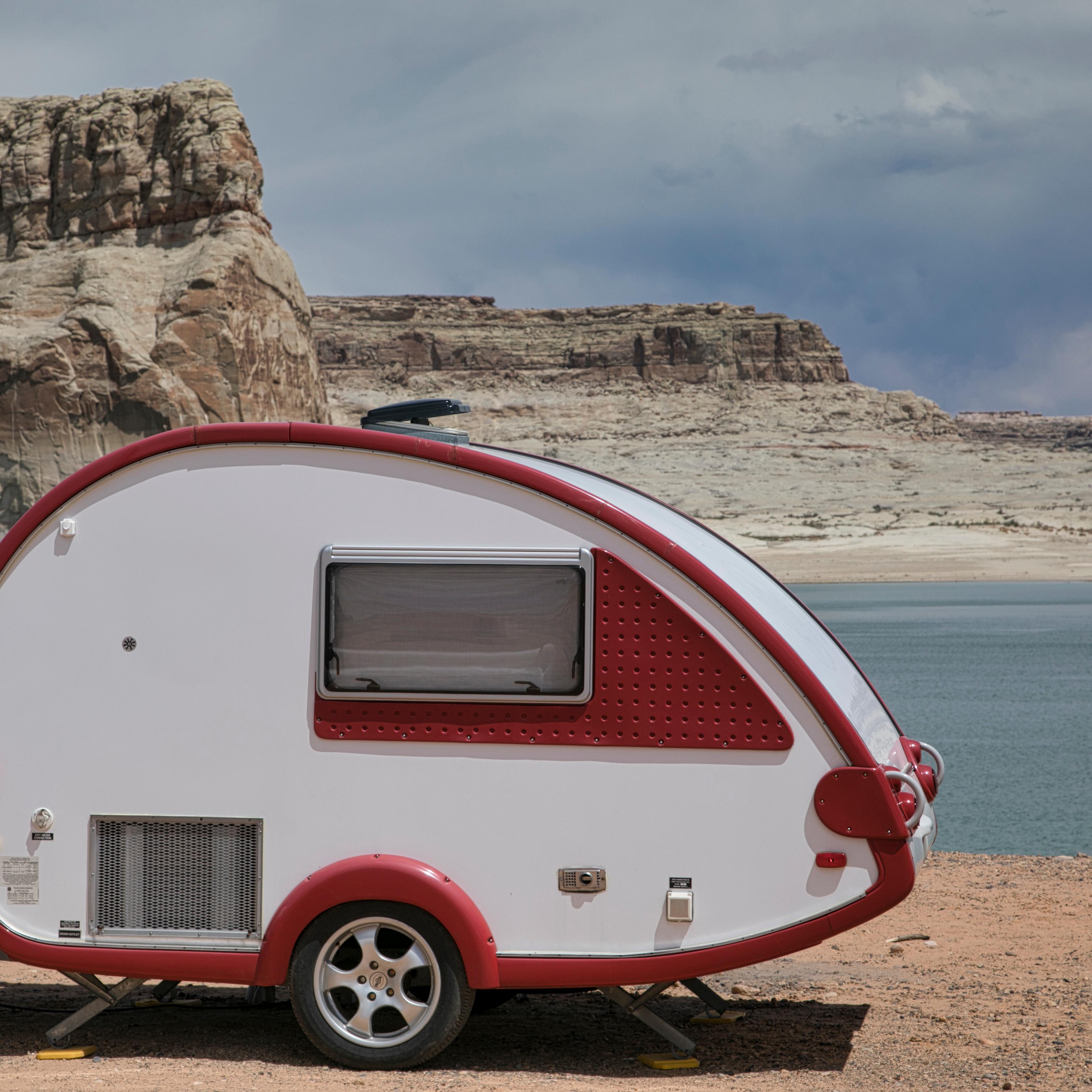 Teardrop camper parked on on a beach at a desert lake. Large sandstone rock formations in background
