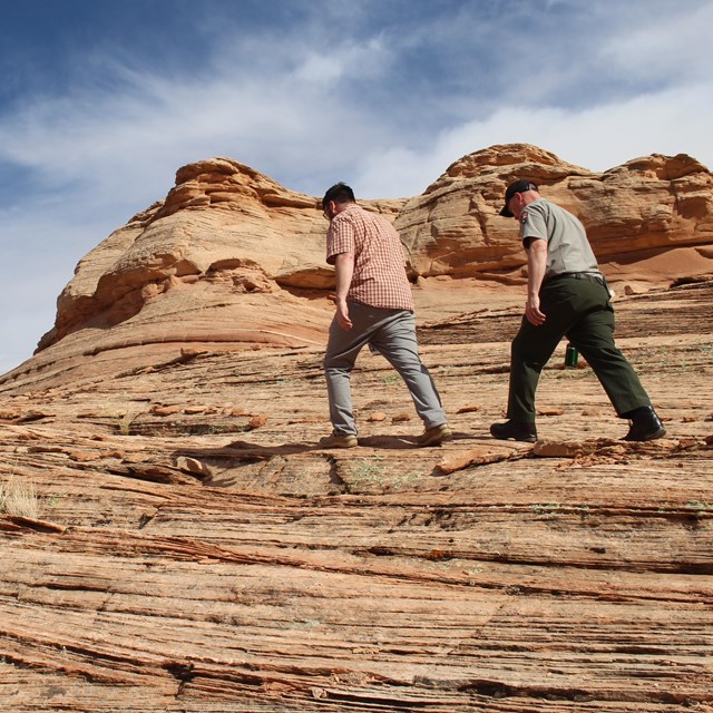 Ranger and visitor hike over twisting, layered sandstone