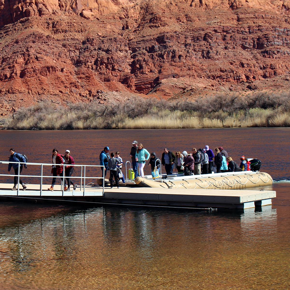 People in a line on a short boat dock board a large rubber raft.
