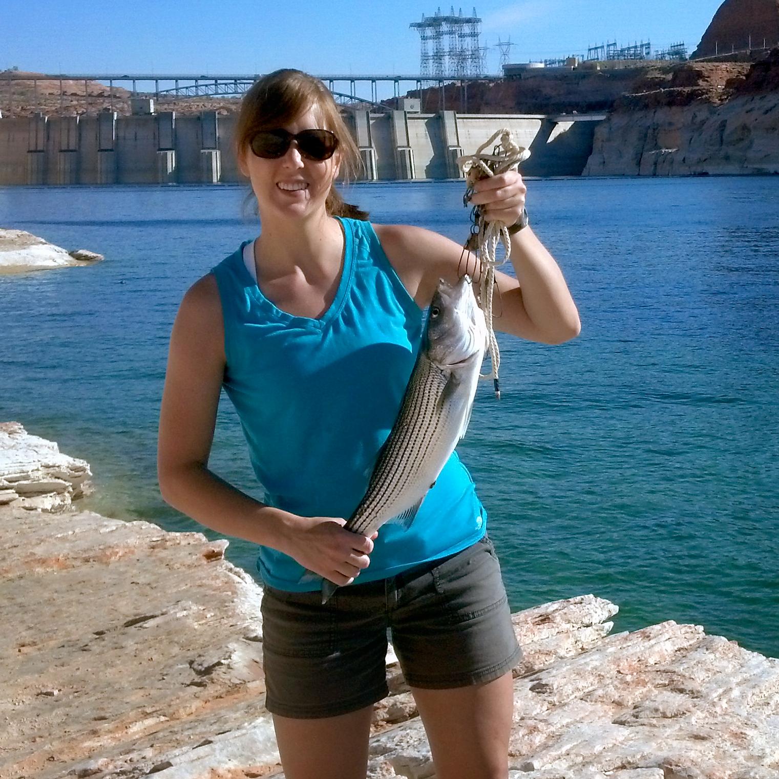 Woman holds up a large striper caught near dam