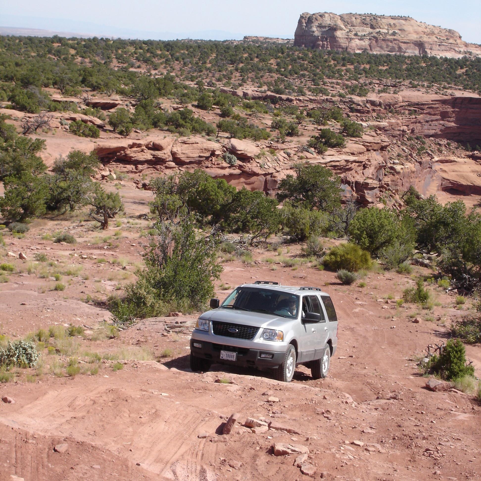 SUV drives over unpaved road with butte behind