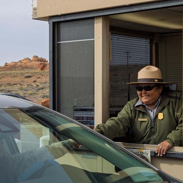 Park Ranger in fee booth reaches out to driver of car.