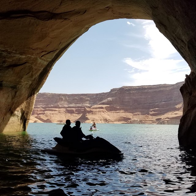 rock arch over water, watercraft in shadow