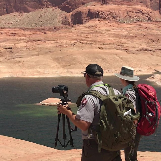 Two rangers, one holding a camera, standing on sandstone cliff