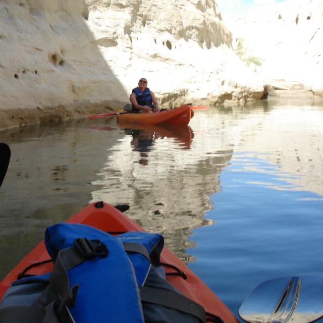 Multicolored kayaks in and out of the shadows on the lake.