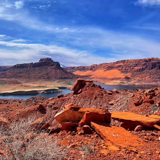 Rocky landscape atop a canyon holding a desert lake in front of buttes and mesas.