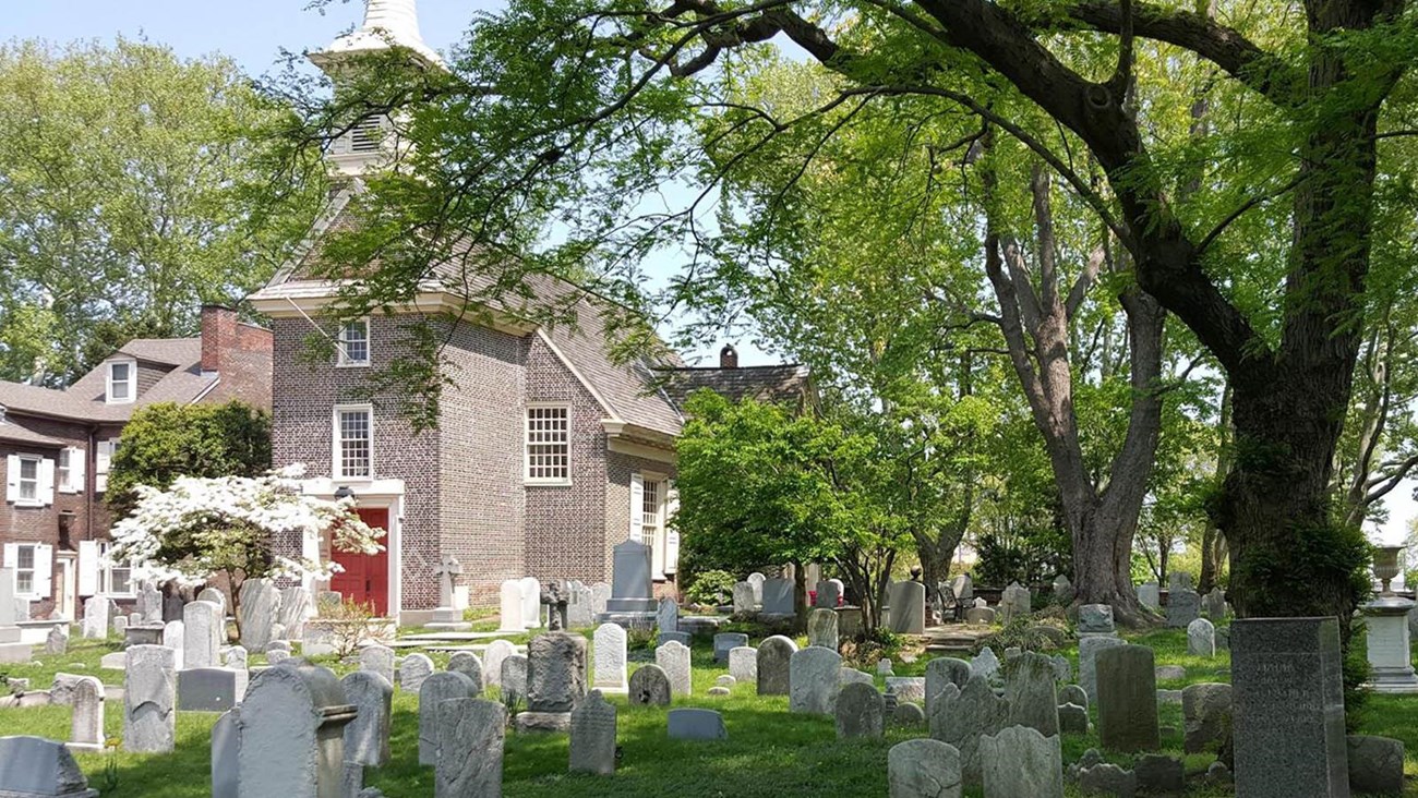 Gloria Dei Burial Ground in the springtime, brick church with wooden steeple in the background.