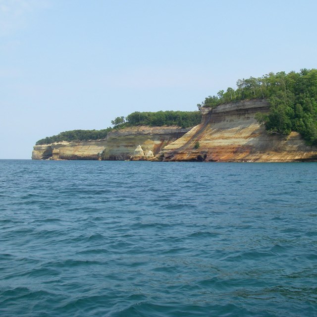 Rust, tan, and gray cliffs at the water's edge