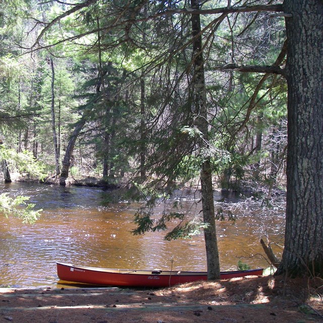 Red canoe on wooded river bank.