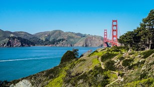 Trails along the bluffs with the a large red suspension bridge crossing a strait in the distance