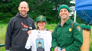 3 park employees stand outside, one holding point bonita t shirt