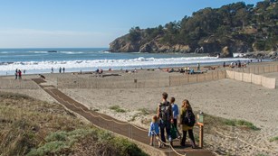 People walking down accessible sand mat onto muir beach with the blue ocean beyond