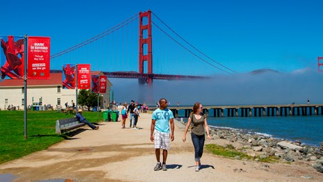 two people walk on Crissy Field with Golden Gate Bridge in the background