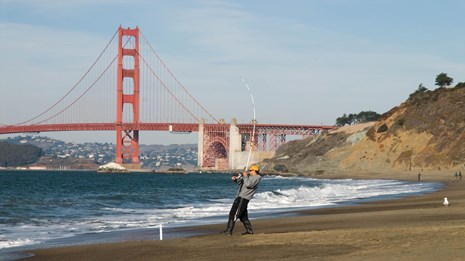 Man fishing on Baker Beach with bridge in background