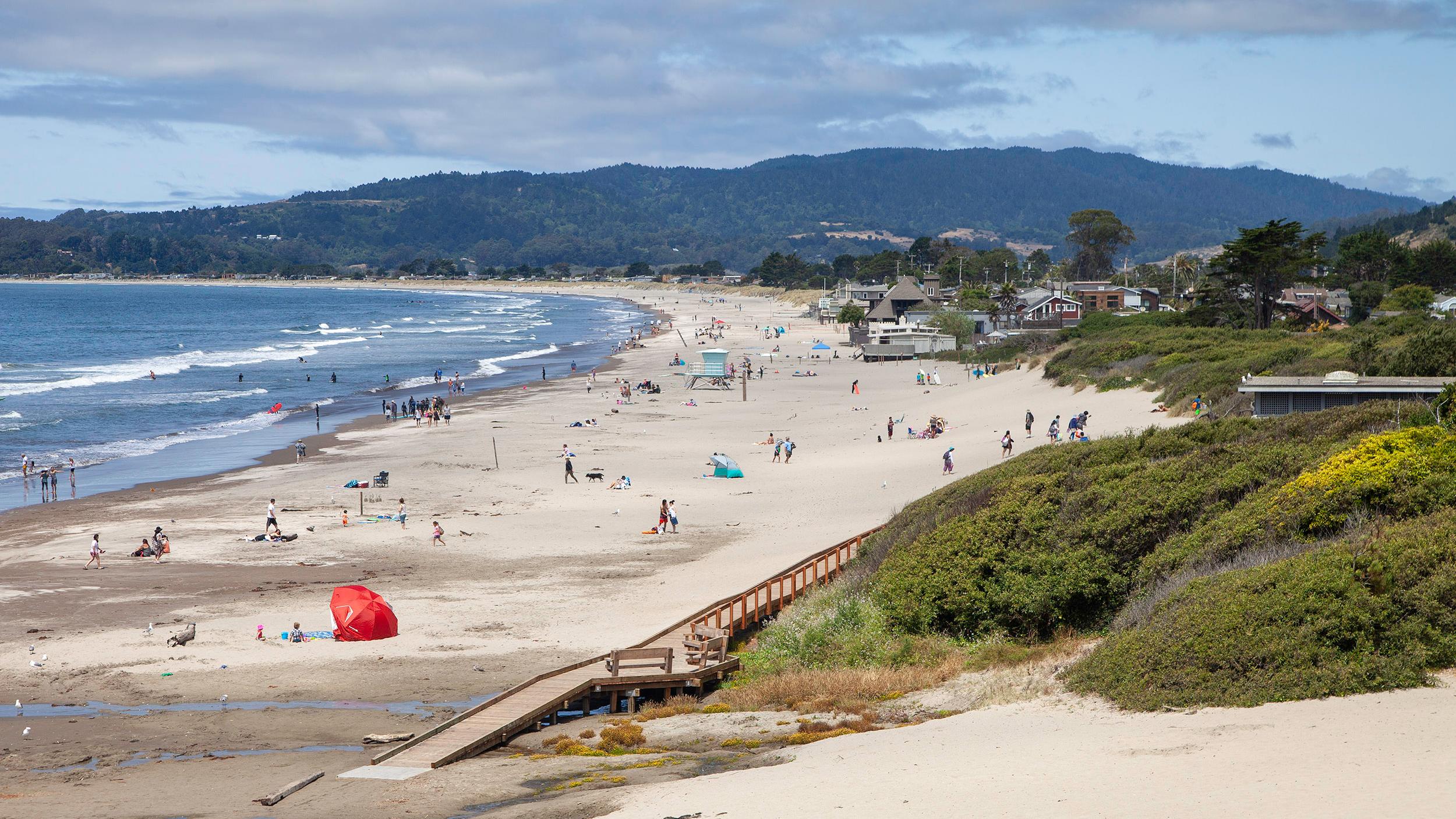 Broad white sand beach with people and forested ridge behind