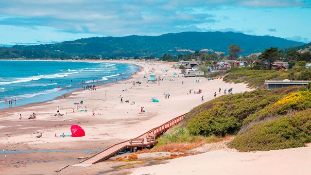 Broad white sand beach with people and forested ridge behind