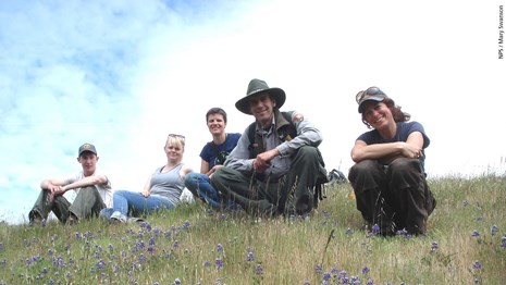 Natural resources staff and volunteers pause for a photo on a flower-filled hillside.