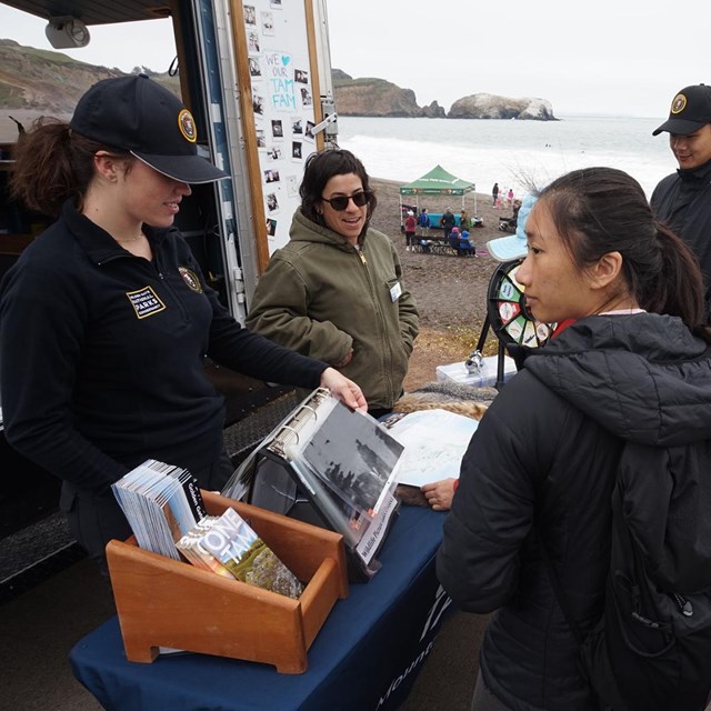 Volunteer at an info table showing visitors park resources while tabling at Rodea Beach.